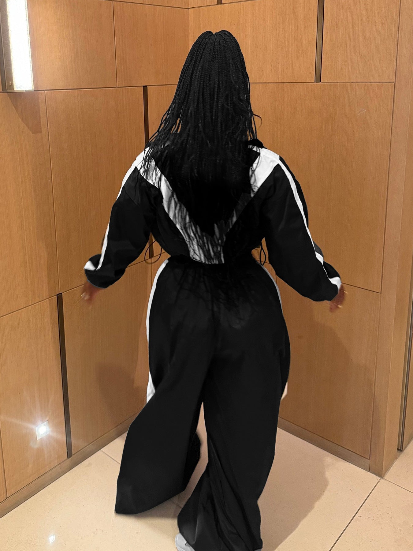 Person wearing a black and white outfit against a wooden wall.