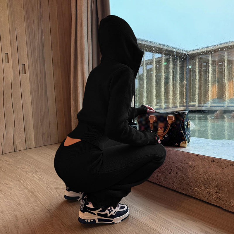 Person in black hoodie and pants squatting by a window with a handbag.