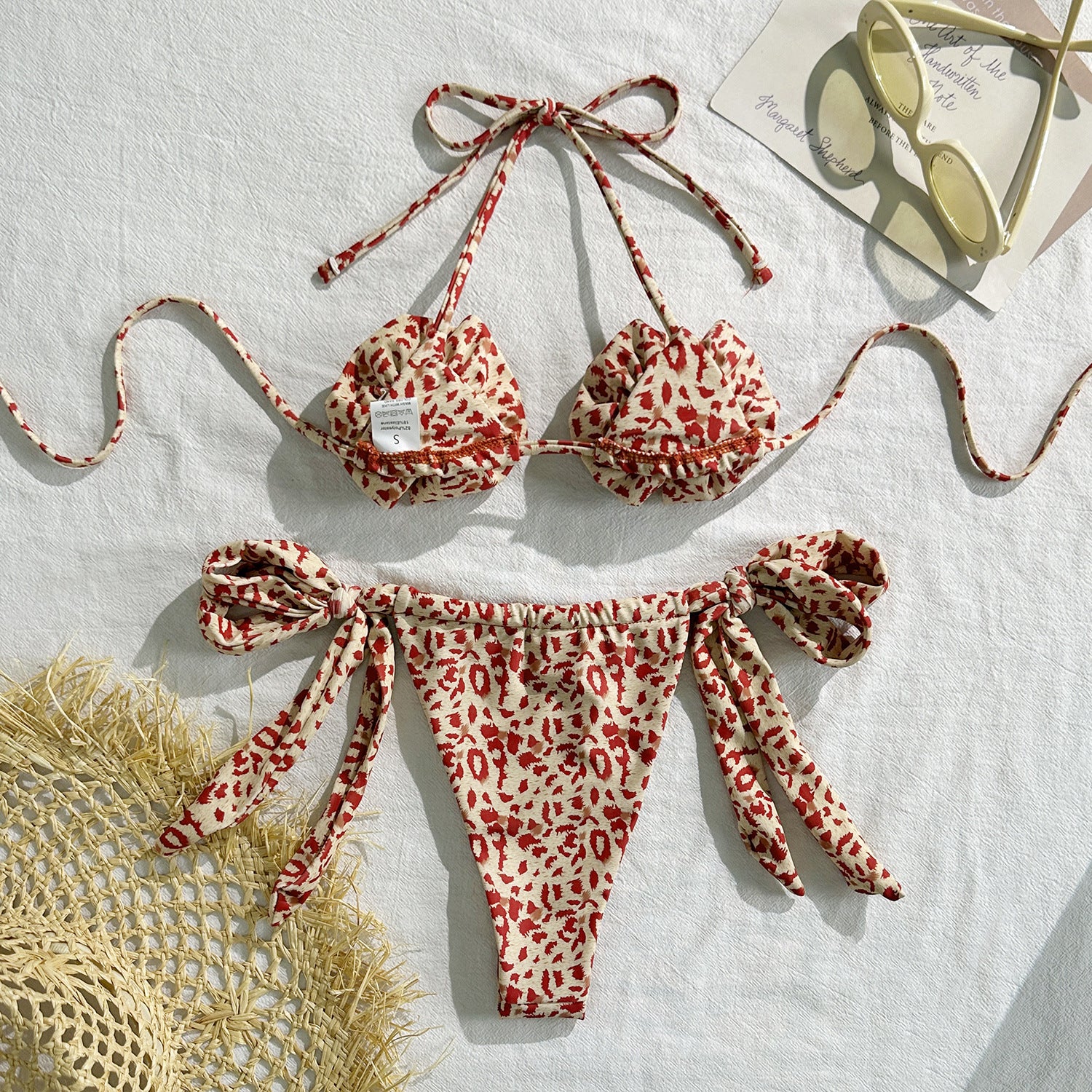 Red and white patterned bikini set on a light background with sunglasses and a hat.